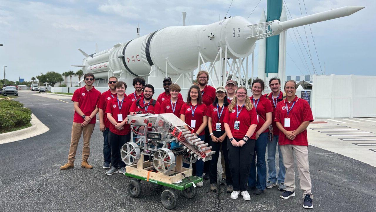 The University of Alabama Astrobotics team stands in front of a rocket with their winning lunar mining rover